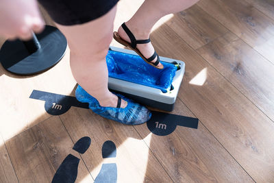 From above of crop anonymous female visitor stepping on automatic device for shoe covers placed at entrance on clinic