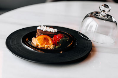 Delicious dessert chocolate piece of cake with fresh strawberry and orange on a black plate