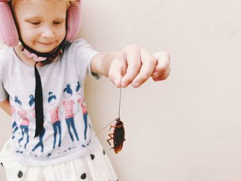 Cute girl holding cockroach while standing against wall