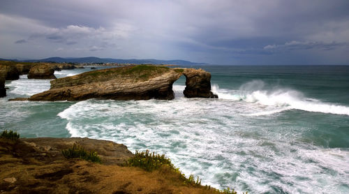 Rock formation at catedrais beach against cloudy sky