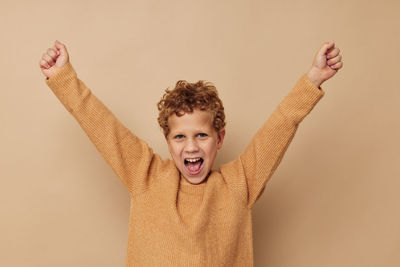 Portrait of smiling boy with arms raised against beige background