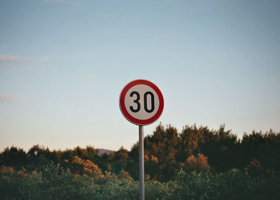 Speed limit sign by trees against sky