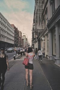 Rear view of people walking on street amidst buildings in city