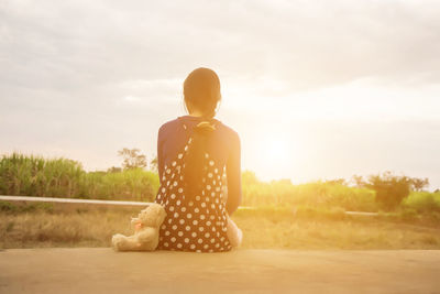 Rear view of woman sitting on field against sky