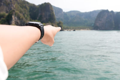 Cropped hand pointing towards sea by mountains