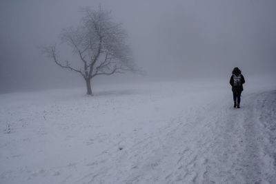 Rear view of man walking on snow covered field