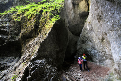 Mother and daughter walking towards cave in rocky mountain