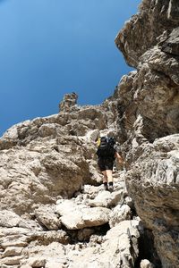 Low angle view of people on rock by mountain against sky