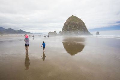 Rear view of people walking on beach against sky