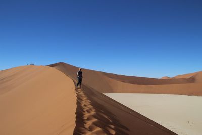 Man standing on sand dune against clear blue sky