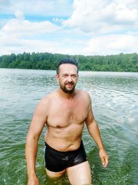 Portrait of shirtless man standing against river