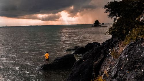 High angle view of man standing on rock by sea against sky