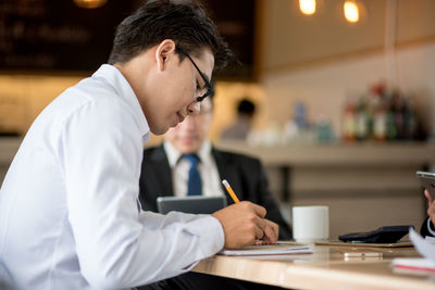 Man holding coffee cup while working on table at cafe