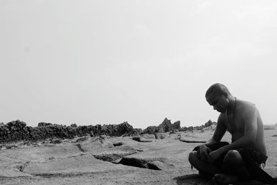 Man sitting on rock against sky