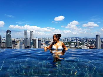 Young woman in infinity pool against cityscape