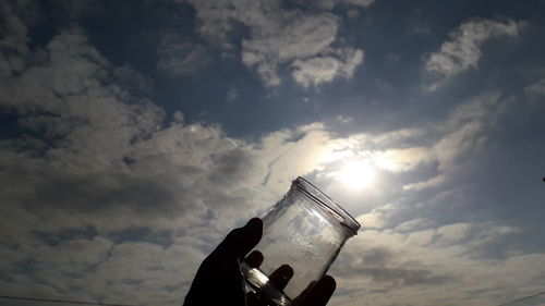 Low angle view of hand holding glass against sky