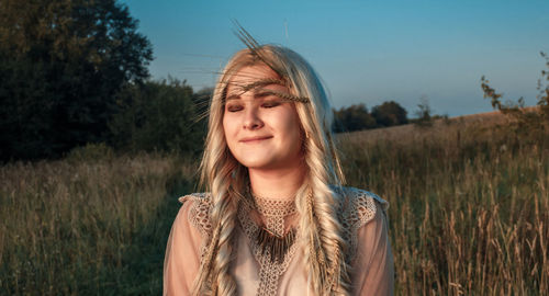 Portrait of beautiful woman standing on field against sky