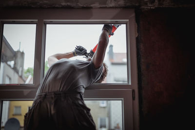 One young builder is repairing a window frame from the outside. person