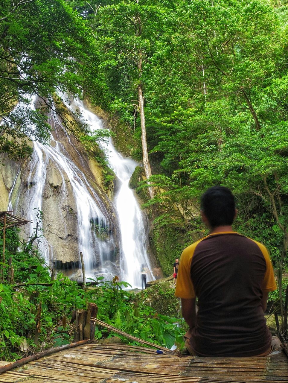 REAR VIEW OF WOMAN SITTING ON WATERFALL IN FOREST