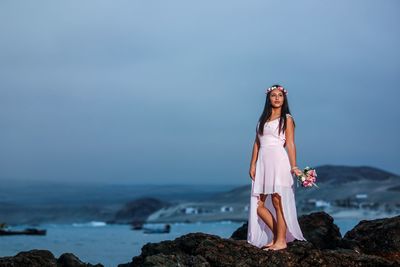 Young woman standing on rock by sea against clear sky