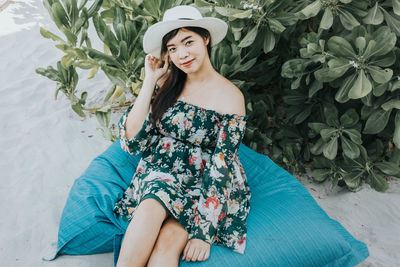 Portrait of smiling woman wearing hat sitting at beach