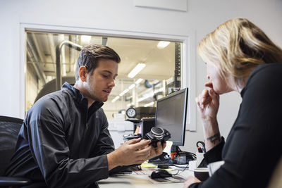 Male owner showing spare part to female customer in office