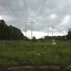 Electricity pylon on field against cloudy sky