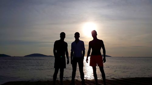 Rear view of silhouette people on beach against sky during sunset