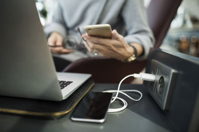 Midsection of businesswoman using smart phone at airport lobby