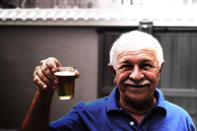 Portrait of senior man holding beer glass outside house