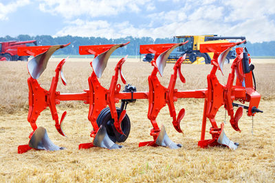 A metal multi-row plow of red color on a blurred background of wheat harvesting with large combines.
