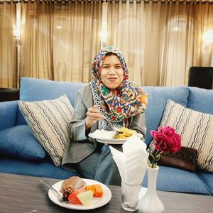 Portrait of woman having food while sitting on sofa at home