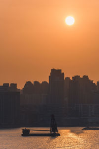 Silhouette buildings by sea against sky during sunset