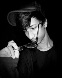 Portrait of young man holding eyeglasses against black background