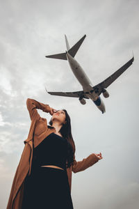 Low angle view of woman standing by airplane against sky