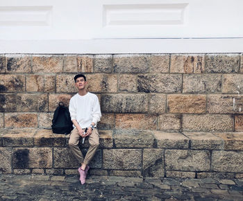 Portrait of young man sitting on staircase against wall