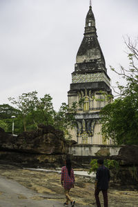 Rear view of people walking outside temple against sky