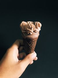 Hand holding ice cream cone against black background