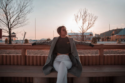 Woman sitting on bench against sky during sunset