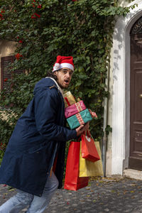 Young man with santa claus hat has a surprised expression and brings his newly purchased gifts.