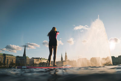 Rear view of woman standing in city against sky during sunset