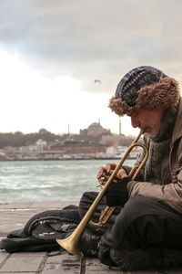 Man playing trumpet in city against sky