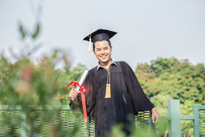 Portrait of smiling student wearing graduation gown while standing in park