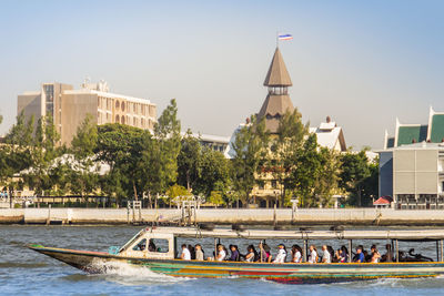 People by boats in river against buildings