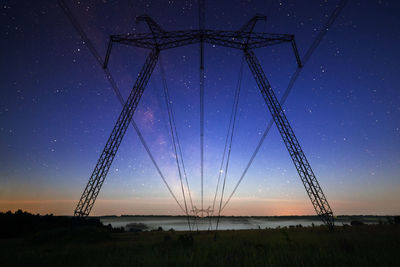 Low angle view of power line towers silhouette on field against starry night sky at summer