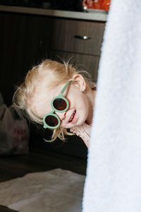 Little 3 years old girl with green glasses looking behind the wall