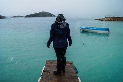 Rear view of woman standing on pier over sea during snowfall