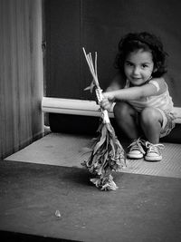 Portrait of girl holding dry plants while crouching against wall
