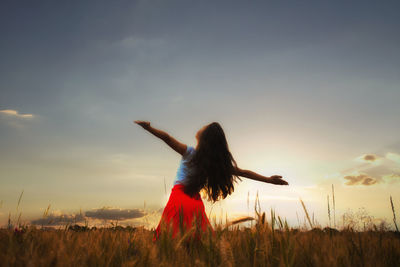 Rear view of woman standing on field against sky during sunset