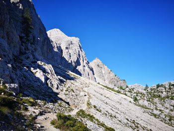 Low angle view of rocky mountains against clear blue sky